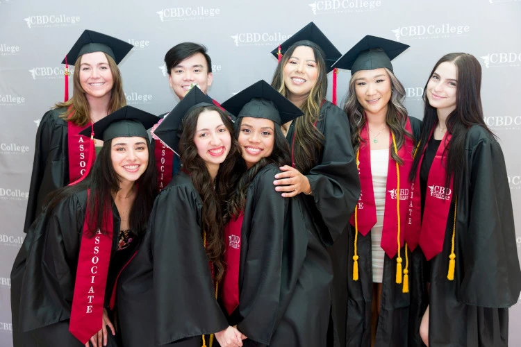 A jubilant group of CBDCollege graduates, beams with happiness, celebrating their academic achievement. In the background, a wall proudly displays the college's logo, symbolizing the culmination of their educational journey.